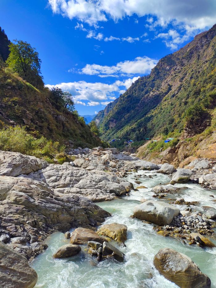 A picturesque mountain river flows through rugged terrain under a blue sky in Vera, India.